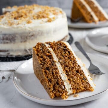 slice of carrot cake on plate with cake in background