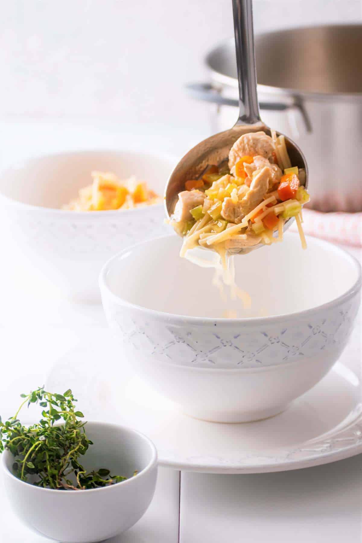 ladle pouring chicken fideo soup into white bowl