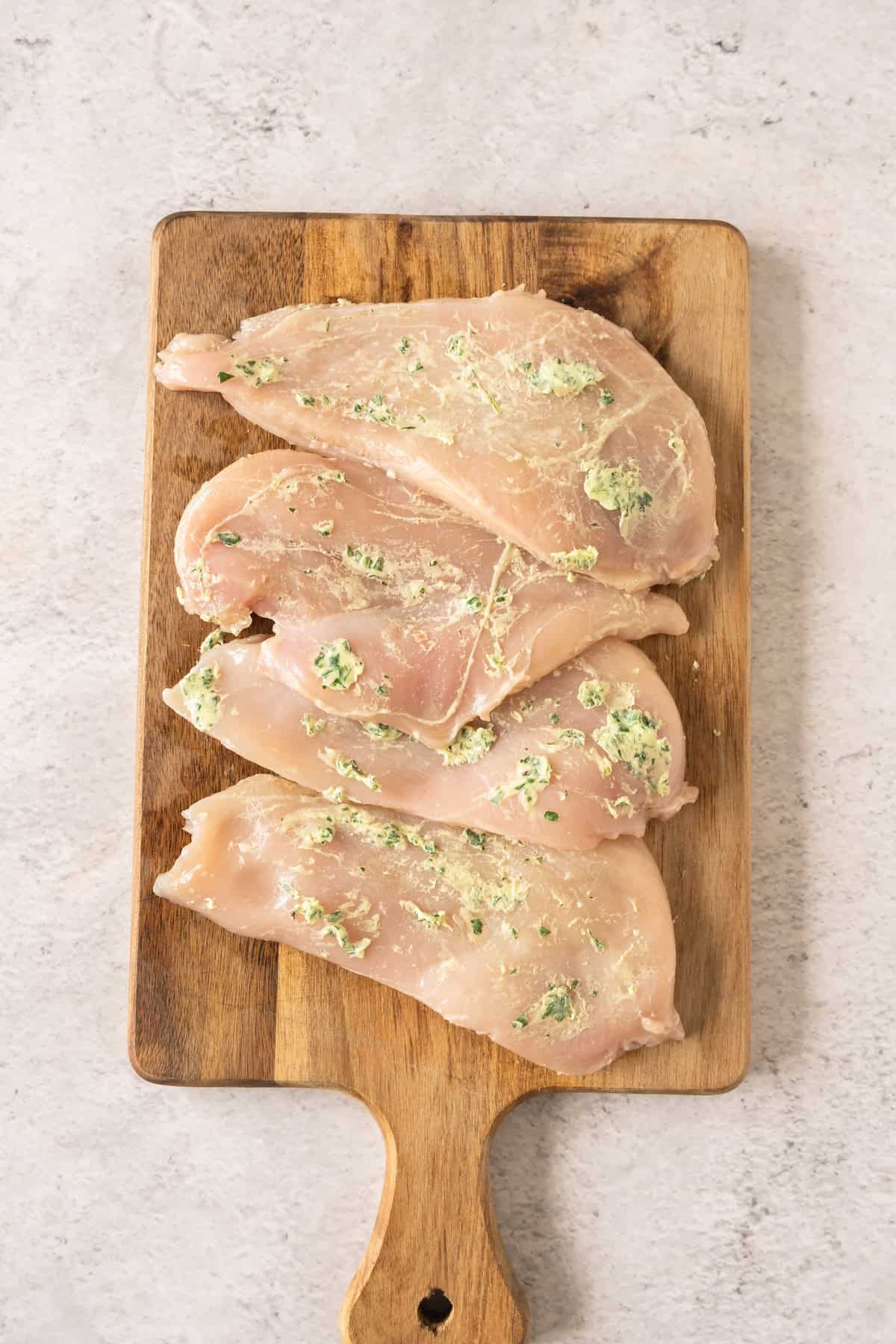 chicken coated with garlic butter laying on cutting board