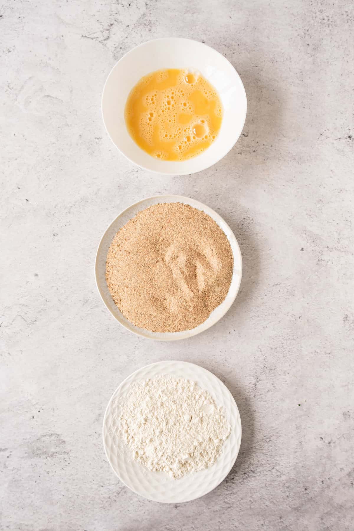 three bowls containing eggs flour and bread crumbs