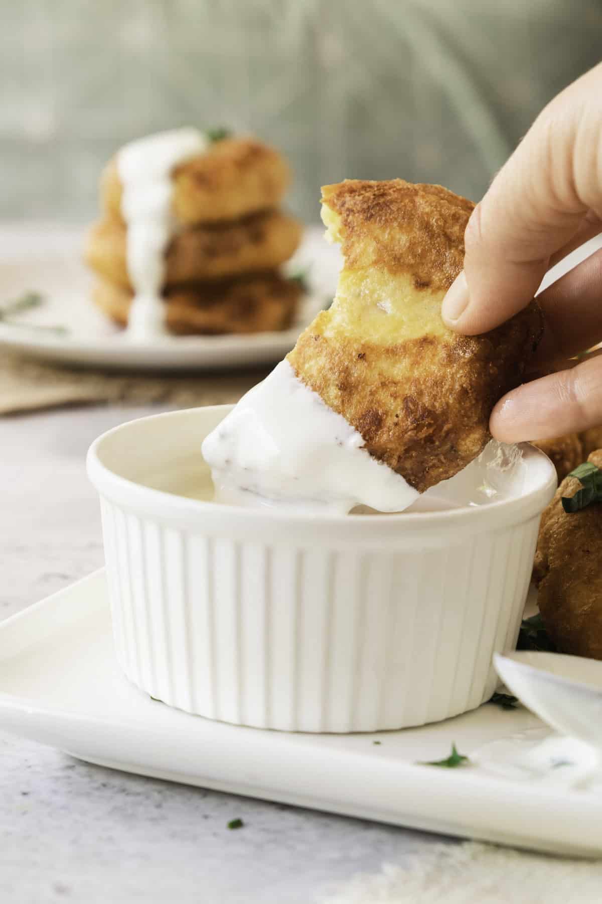 hand dipping potato fritter in sour cream